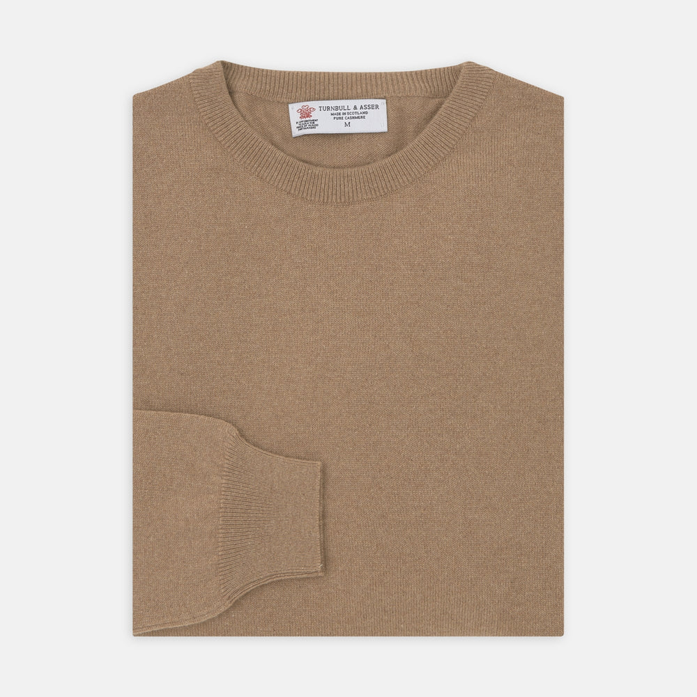 A folded Natural Crew Neck Cashmere Jumper by Turnbull & Asser, in light brown, features a visible brand label and one sleeve neatly laid across the front of this smart casual luxury Scottish sweater.
