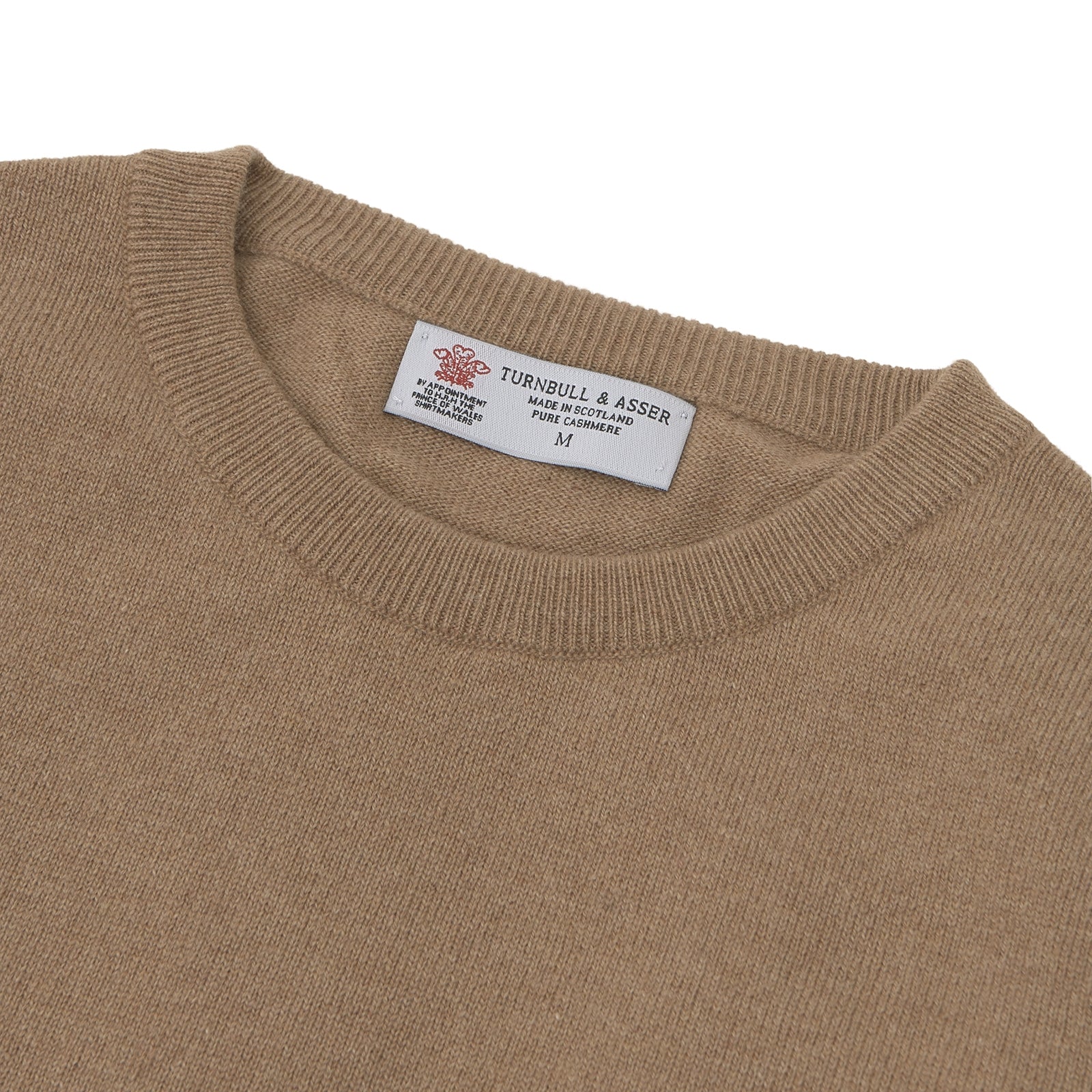 View 4 of product A folded Natural Crew Neck Cashmere Jumper by Turnbull & Asser, in light brown, features a visible brand label and one sleeve neatly laid across the front of this smart casual luxury Scottish sweater.