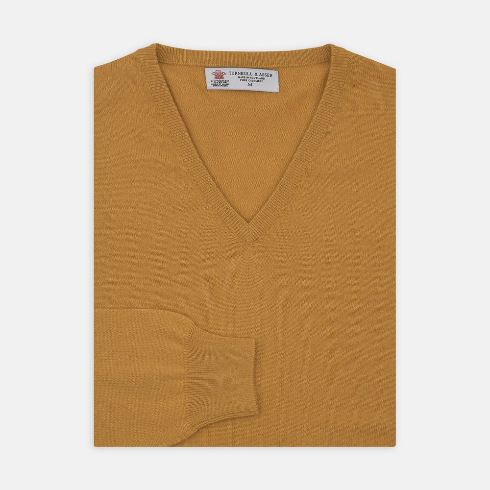 A Sunflower Yellow V-Neck Cashmere Jumper by Turnbull & Asser is neatly folded on a white background, with ribbed cuffs and a visible branded collar label, showcasing this luxurious knitwear piece.