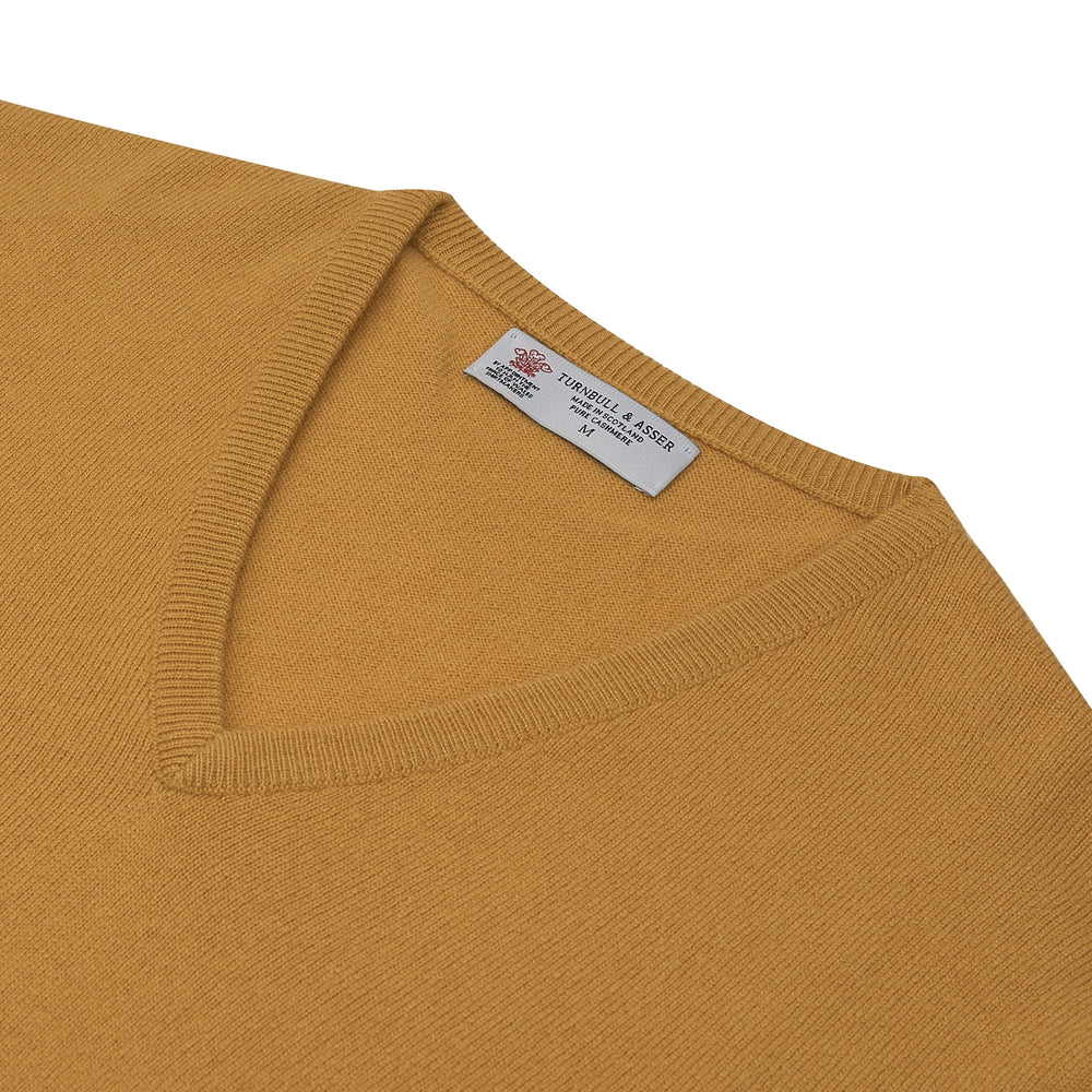 A Sunflower Yellow V-Neck Cashmere Jumper by Turnbull & Asser is neatly folded on a white background, with ribbed cuffs and a visible branded collar label, showcasing this luxurious knitwear piece.