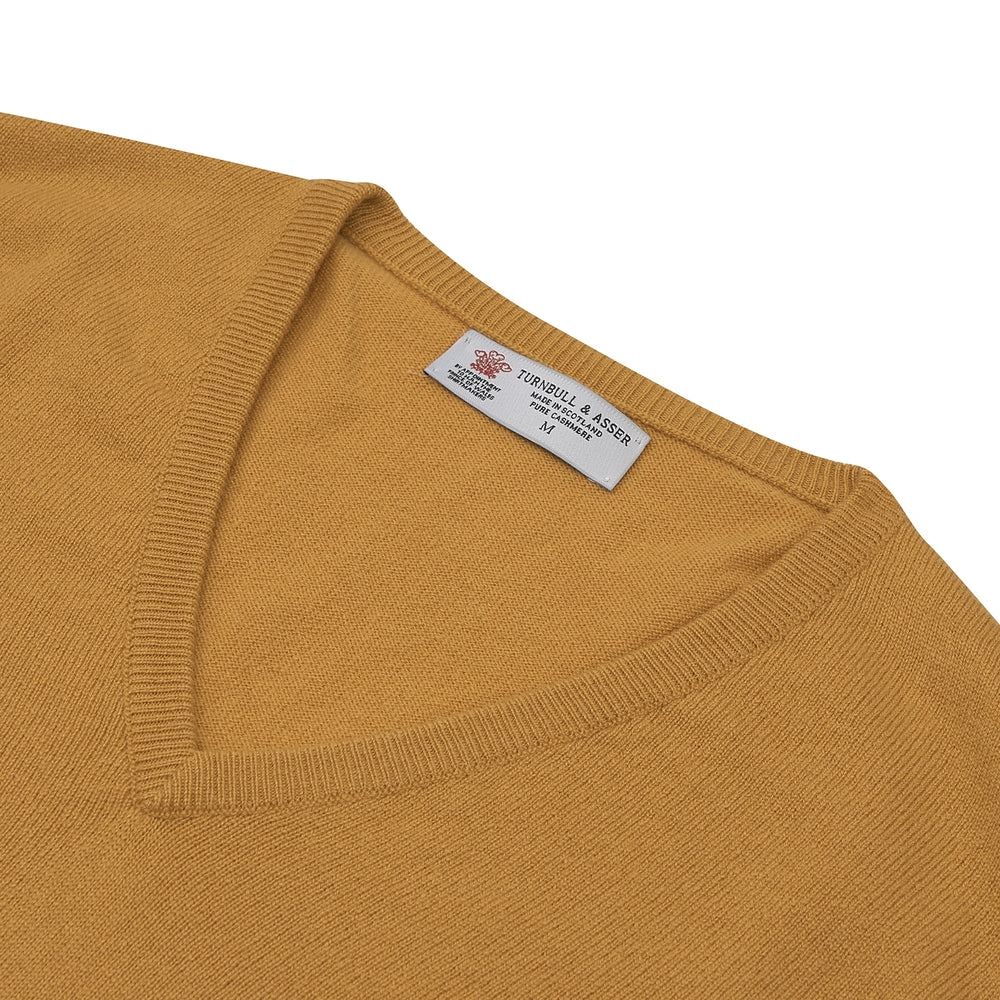 The Sunflower Yellow V-Neck Cashmere Slipover by Turnbull & Asser is neatly folded on a white background, showing the front and label—ideal for formal layering or as a versatile cashmere addition to your wardrobe.