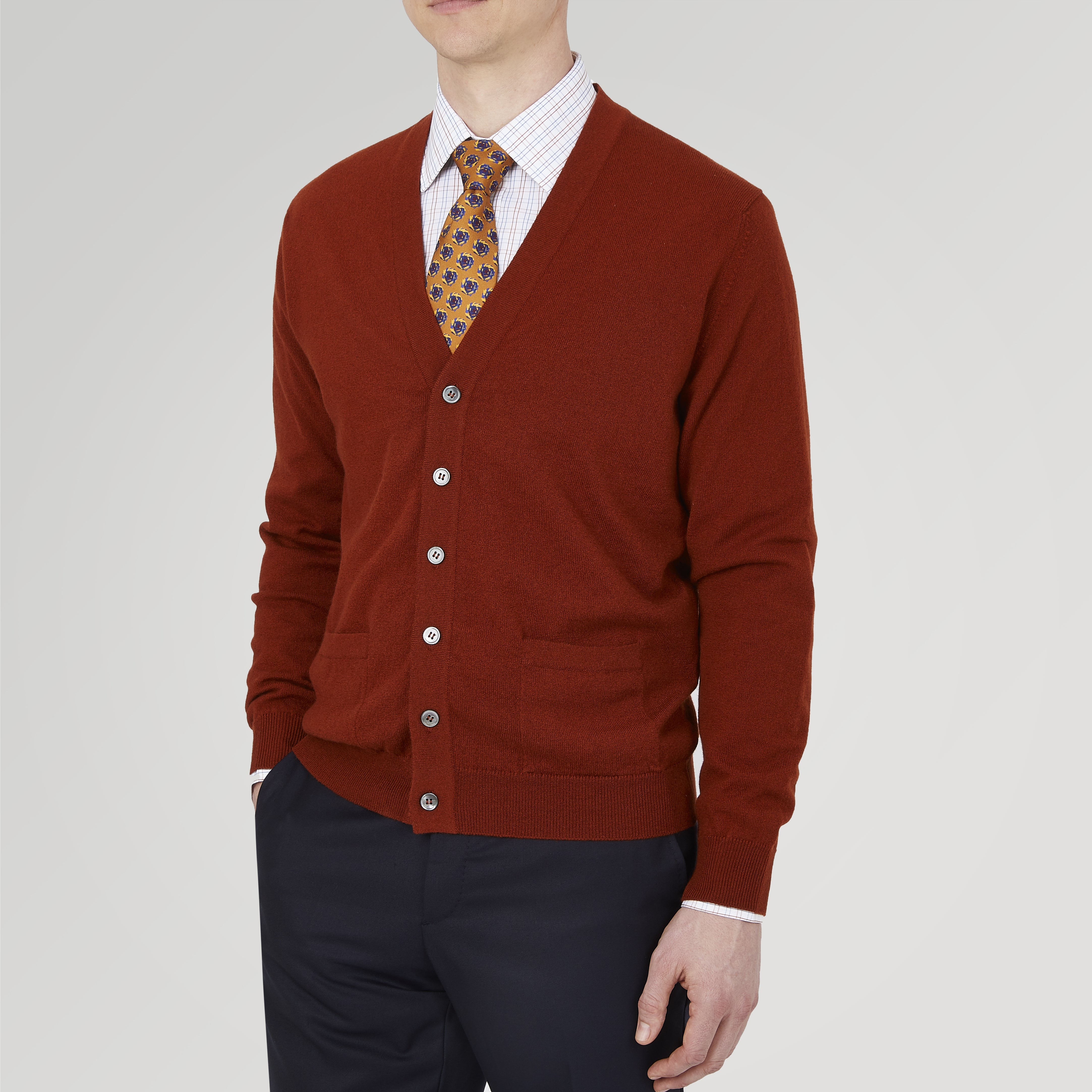 View 2 of product The Harissa Cashmere Cardigan by Turnbull & Asser, in deep red-brown 21GG knit, is folded to display its V-neck, ribbed cuffs, and two buttons against a white background.