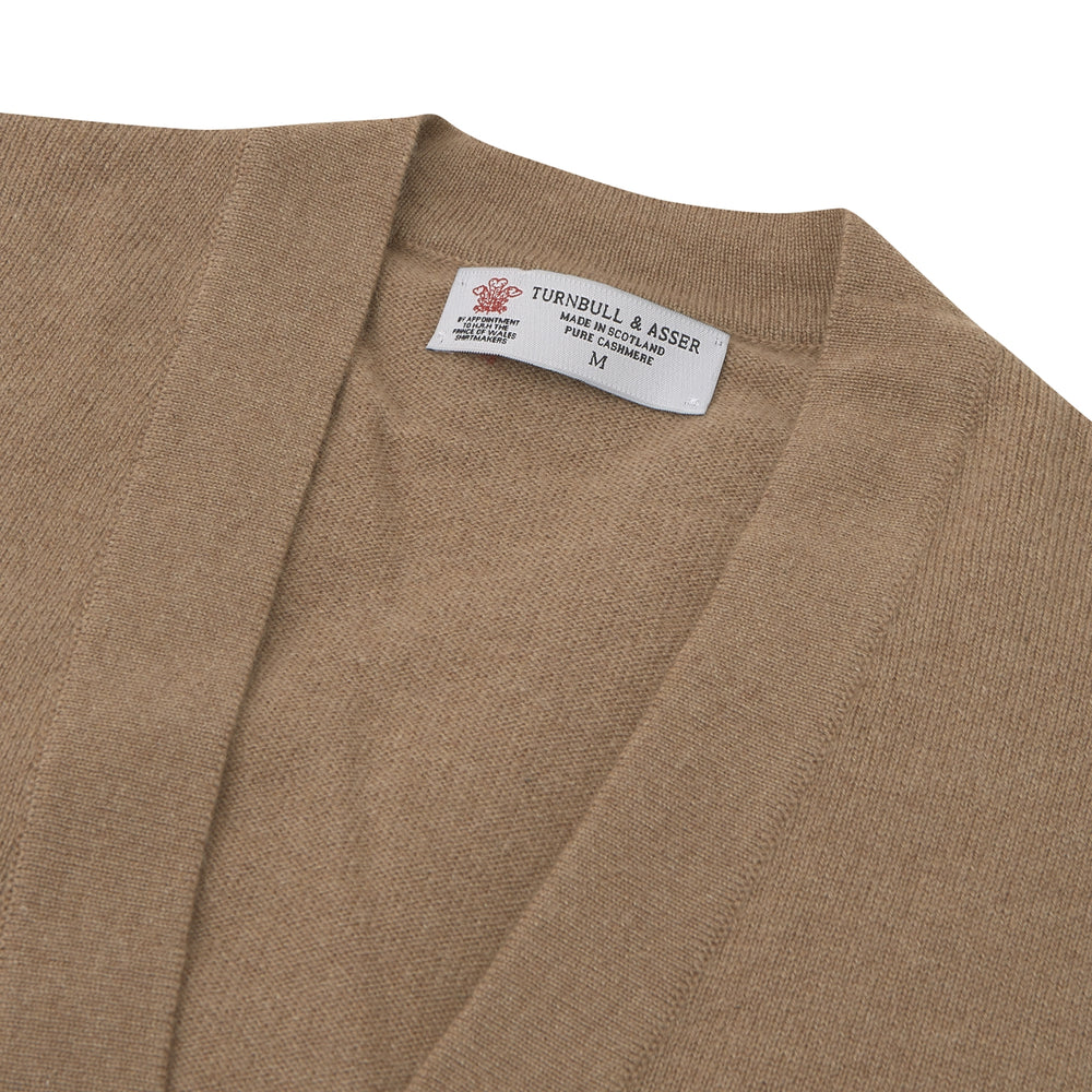 A Natural Cashmere Cardigan by Turnbull & Asser, light brown with a V-neckline, ribbed cuffs, and button closure, is neatly folded and displayed against a white background.