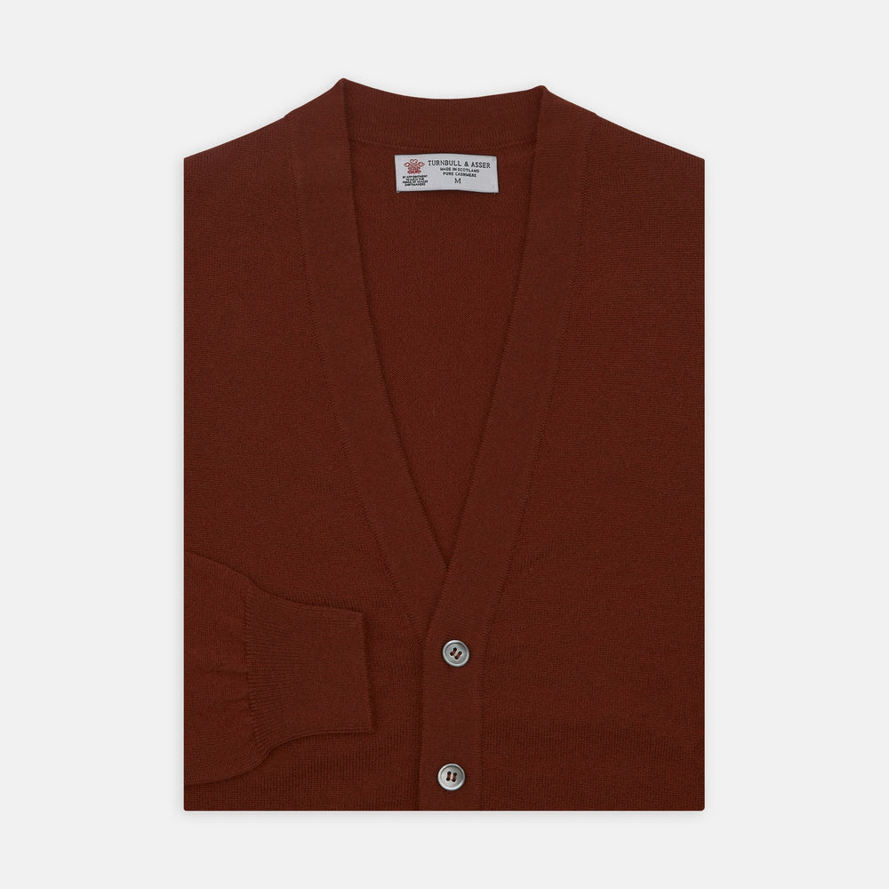 The Harissa Cashmere Cardigan by Turnbull & Asser, in deep red-brown 21GG knit, is folded to display its V-neck, ribbed cuffs, and two buttons against a white background.