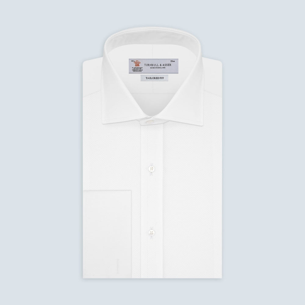 A neatly folded Turnbull & Asser Tailored Fit White Marcella Front Shirt with a Kent collar and double cuffs is displayed against a light grey background, with the label inside the collar visible.