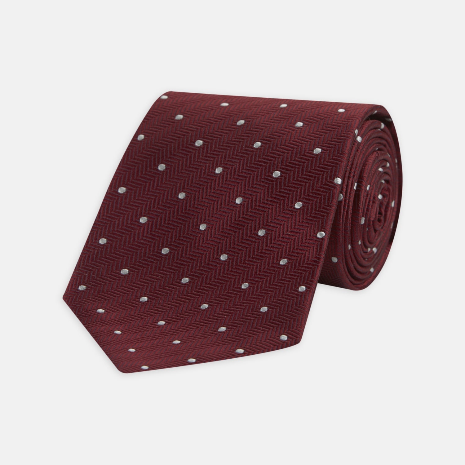 View 1 of product The Turnbull & Asser Burgundy and White Small Spot Herringbone Silk Tie, crafted from fine English silk, is shown rolled up on a plain white background.