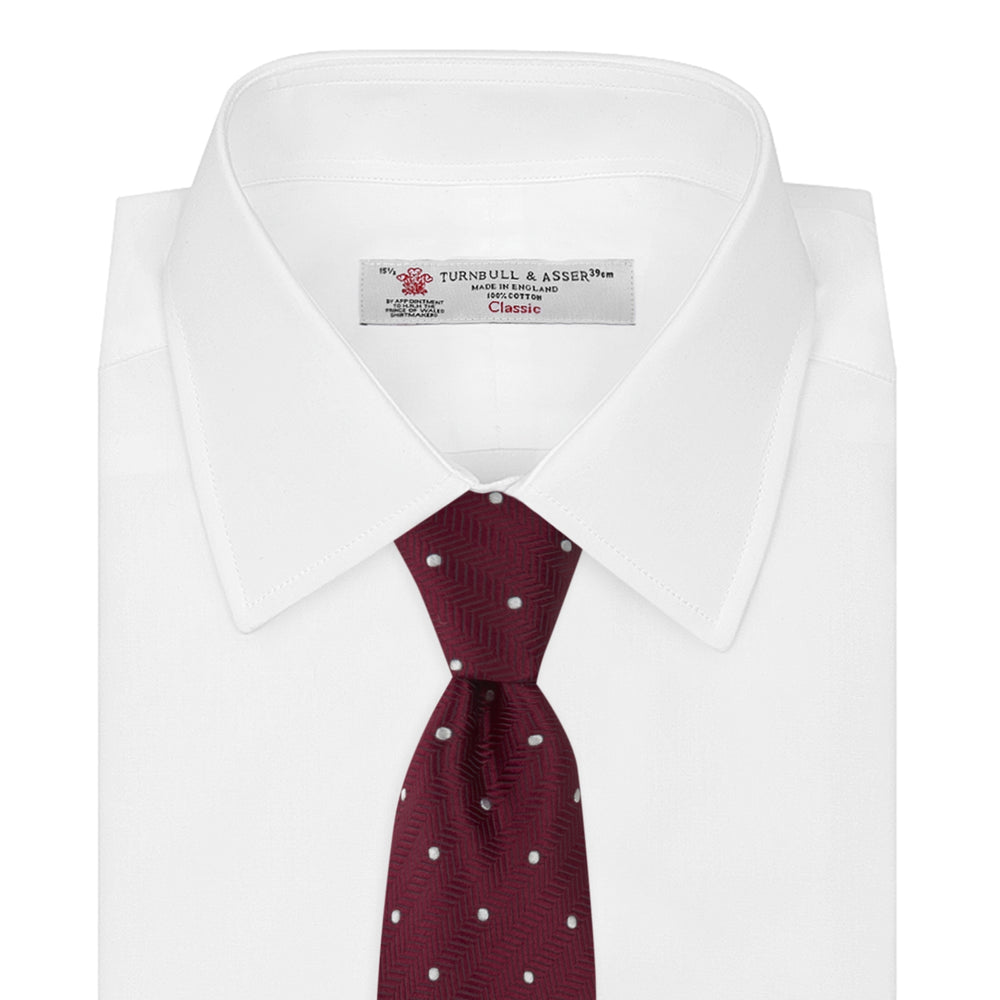 The Turnbull & Asser Burgundy and White Small Spot Herringbone Silk Tie, crafted from fine English silk, is shown rolled up on a plain white background.