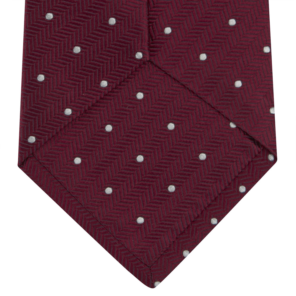 The Turnbull & Asser Burgundy and White Small Spot Herringbone Silk Tie, crafted from fine English silk, is shown rolled up on a plain white background.