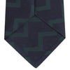 View 4 of product A modern essential, the Turnbull & Asser Navy and Forest Green Striped Zigzag Silk Tie features a bold navy and forest green zigzag pattern, elegantly displayed rolled on a crisp white background.