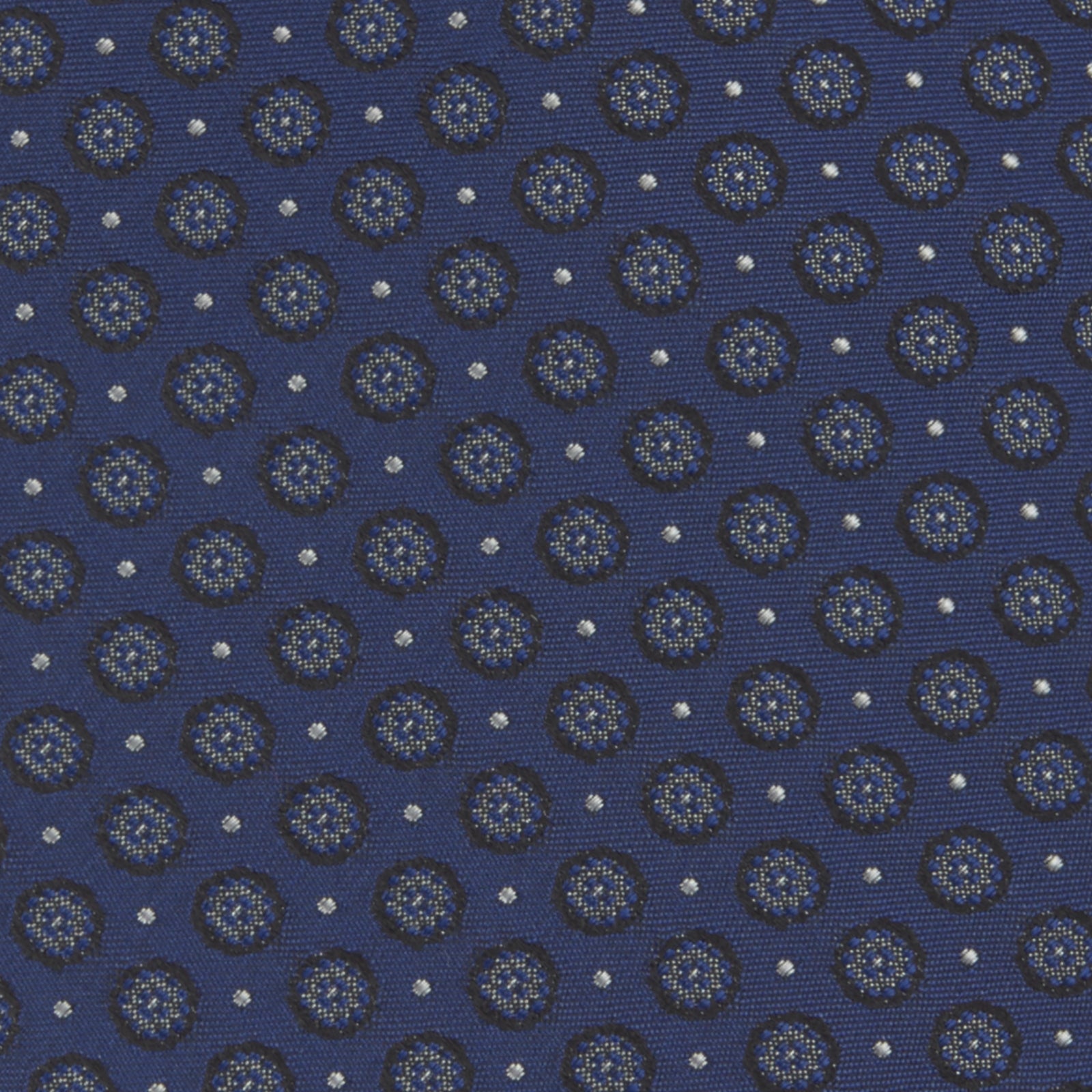 View 3 of product The Turnbull & Asser Navy Floral Spot Silk Tie, featuring a subtle light blue and gray pattern, is rolled up against a plain white background—an ideal accessory for any office shirt.