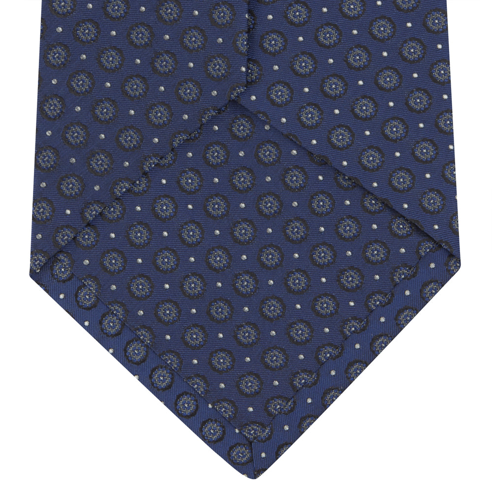 The Turnbull & Asser Navy Floral Spot Silk Tie, featuring a subtle light blue and gray pattern, is rolled up against a plain white background—an ideal accessory for any office shirt.