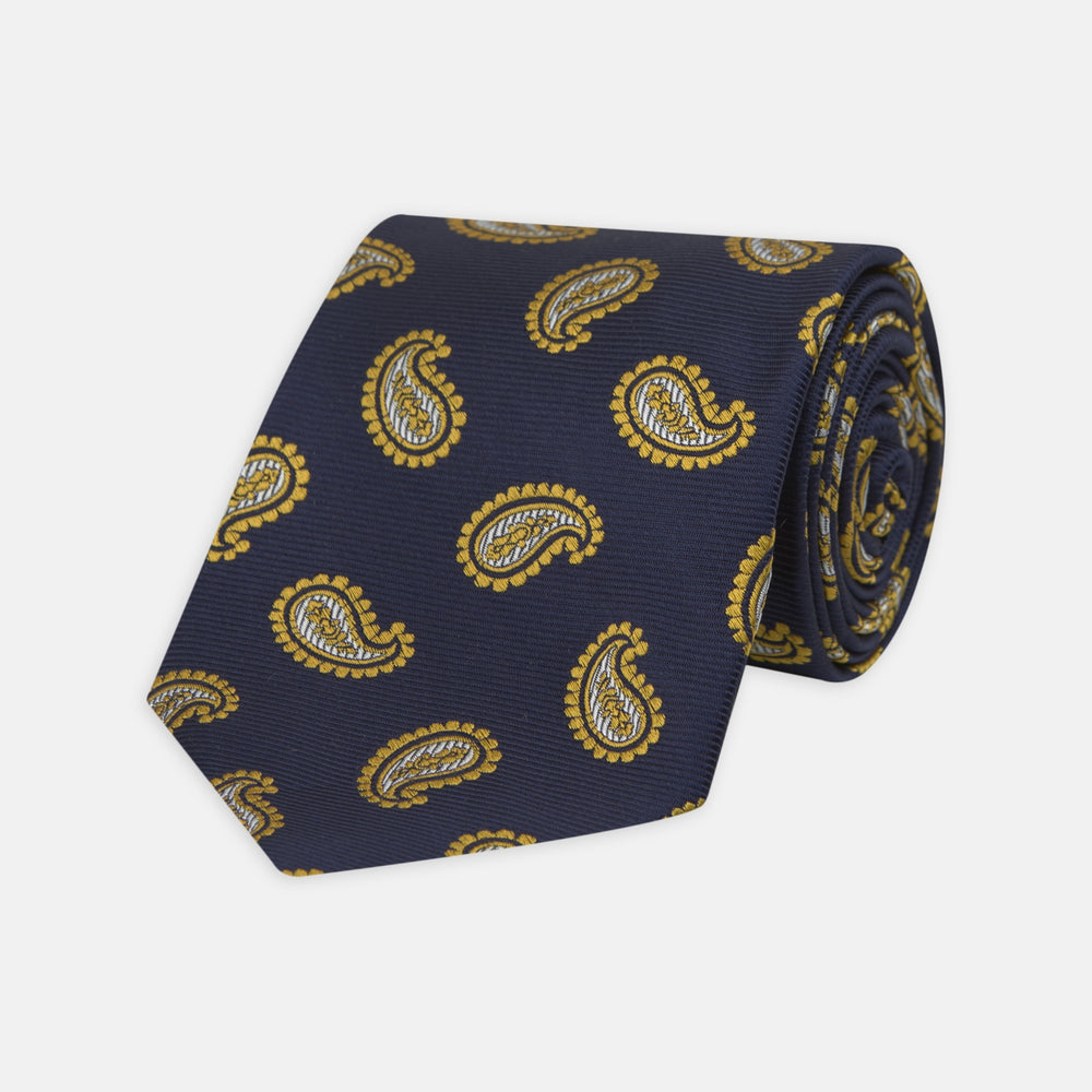 The Turnbull & Asser Navy and Gold Floating Paisley Silk Tie features a repeating yellow and white paisley pattern, shown rolled with the pointed end facing forward against a white background.