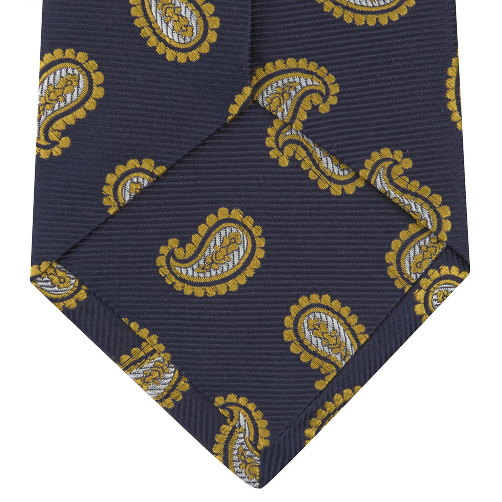 The Turnbull & Asser Navy and Gold Floating Paisley Silk Tie features a repeating yellow and white paisley pattern, shown rolled with the pointed end facing forward against a white background.