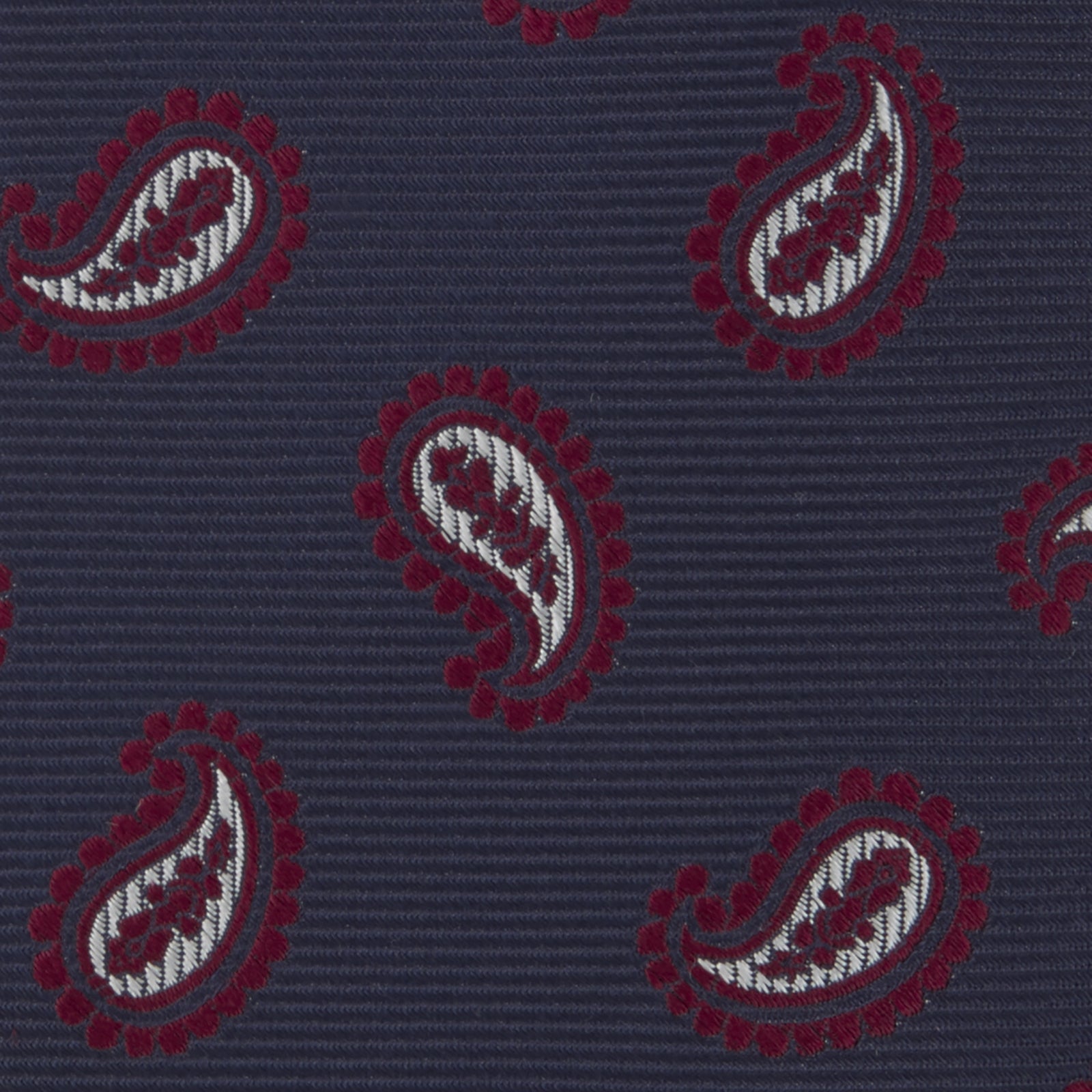 View 3 of product The Turnbull & Asser Navy and Burgundy Floating Paisley Silk Tie is shown rolled up, displaying its repeating paisley design on a plain white background.