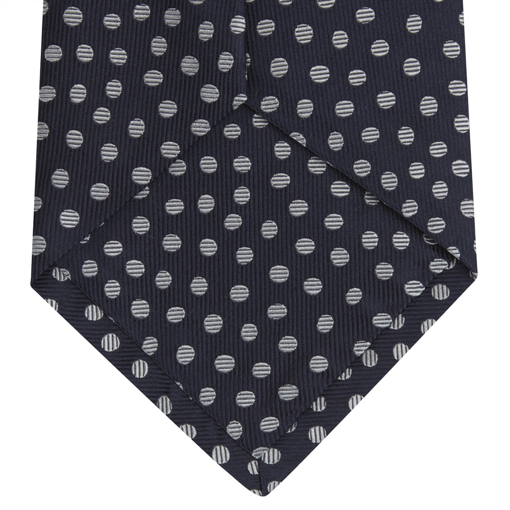 The Turnbull & Asser Navy and White Paint Spot Silk Tie features evenly spaced white spots on classic navy, shown rolled up on a white background—ideal for complementing your favorite office shirt.