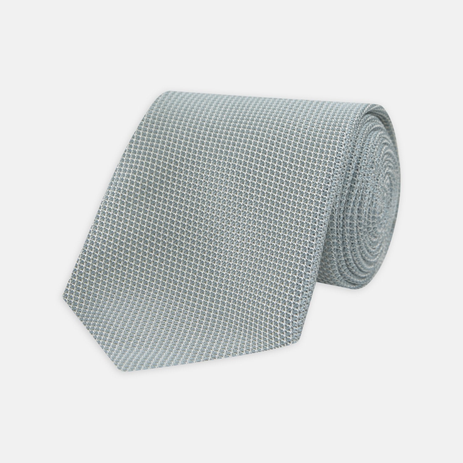 View 1 of product A neatly rolled Turnbull & Asser Light Blue Grenadine Silk Tie, featuring a subtle textured weave, displayed on a white background.