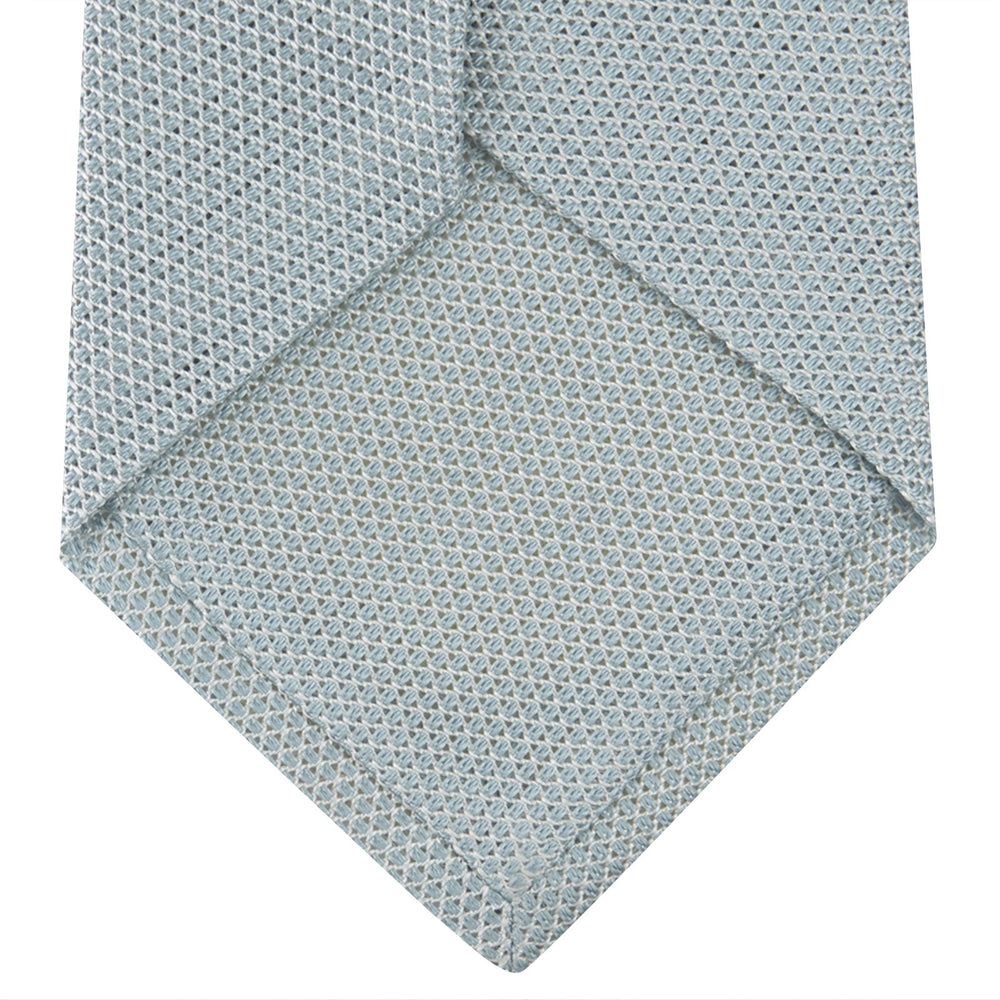 A neatly rolled Turnbull & Asser Light Blue Grenadine Silk Tie, featuring a subtle textured weave, displayed on a white background.