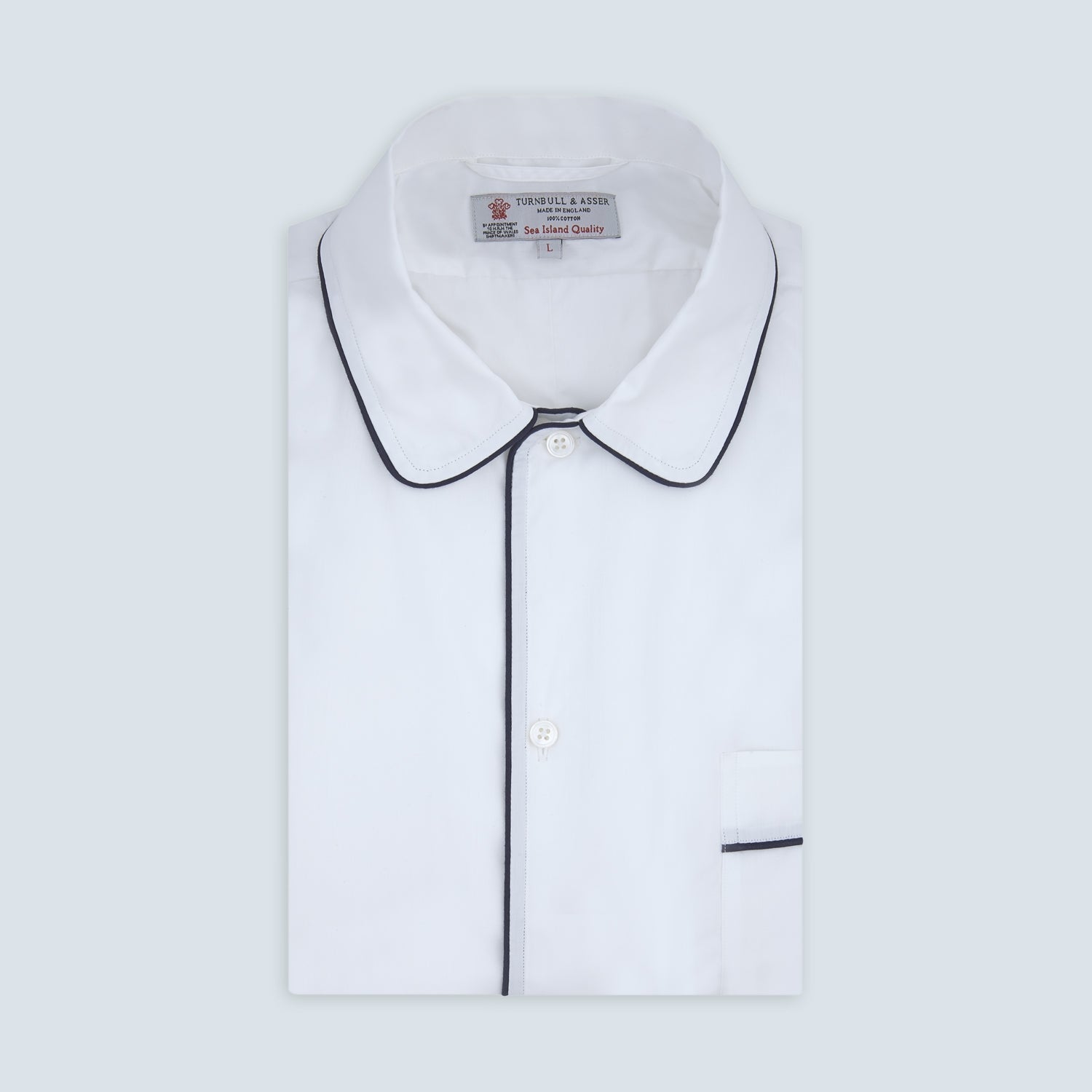 View 1 of product The Turnbull & Asser White Sea Island Quality Cotton Nightshirt, featuring black piping on the collar and pocket, is elegantly displayed folded against a light grey background.