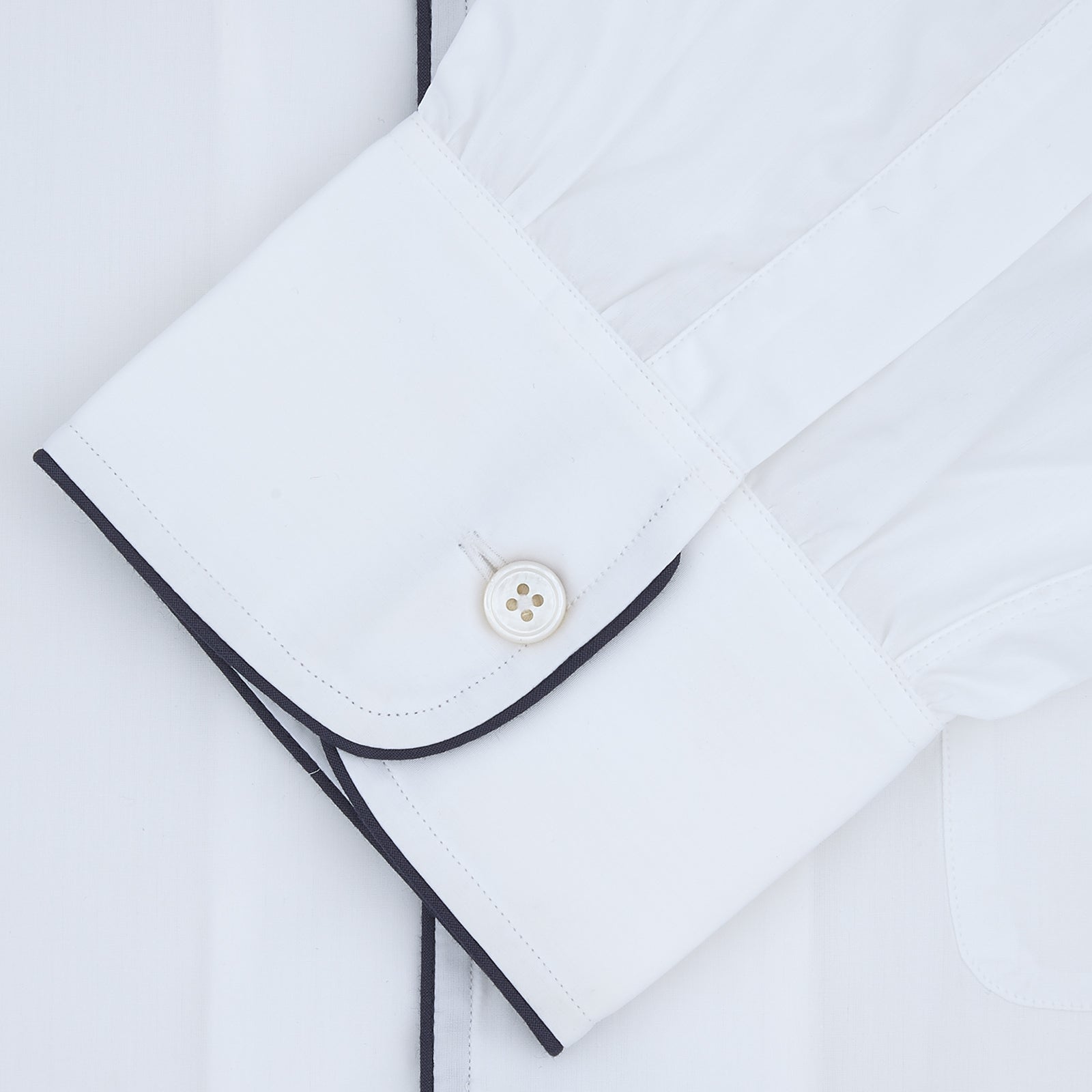 View 2 of product The Turnbull & Asser White Sea Island Quality Cotton Nightshirt, featuring black piping on the collar and pocket, is elegantly displayed folded against a light grey background.