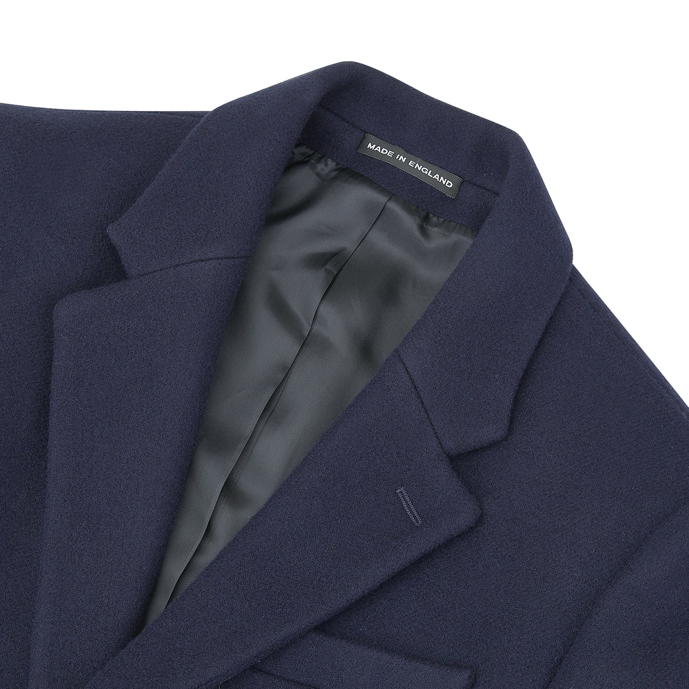 The Turnbull & Asser Navy Lambswool Joseph Overcoat, a men's knee-length coat with notched lapels, a single-breasted front, and three flap pockets per side, is shown against a plain white background.
