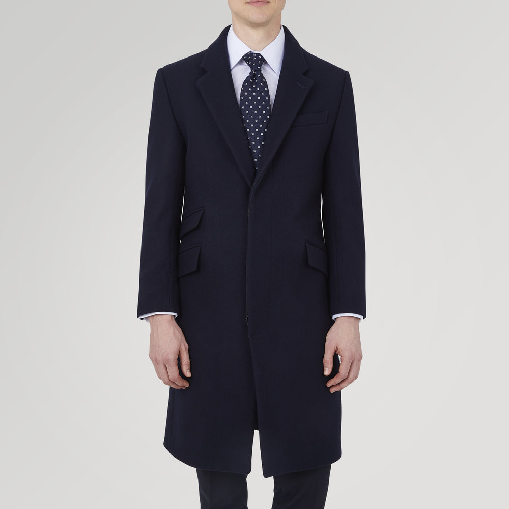 The Turnbull & Asser Navy Lambswool Joseph Overcoat, a men's knee-length coat with notched lapels, a single-breasted front, and three flap pockets per side, is shown against a plain white background.