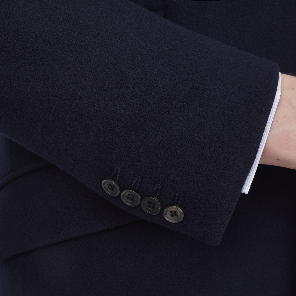 The Turnbull & Asser Navy Lambswool Joseph Overcoat, a men's knee-length coat with notched lapels, a single-breasted front, and three flap pockets per side, is shown against a plain white background.
