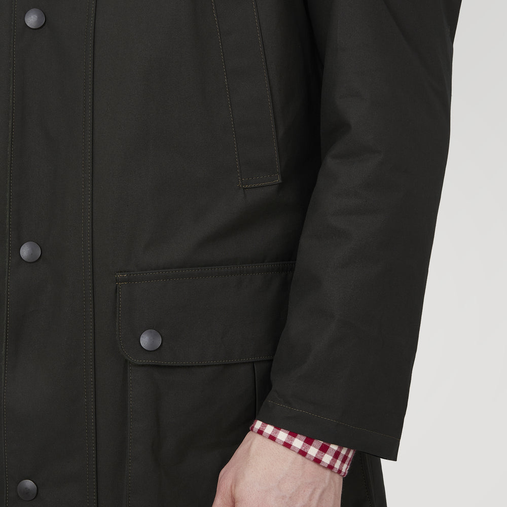 The Turnbull & Asser Dark Green Waxed Cotton Field Coat features a straight fit, button-up front, two large bottom flap pockets, slanted chest pockets, and a contrasting collar. Shown against a plain white background.