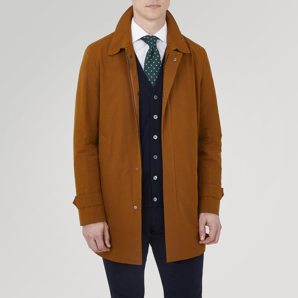 The Turnbull & Asser Dark Khaki Cotton Car Coat features a classic collar, long sleeves, front welt pockets, tailored fit, and concealed button closure in a knee-length modern design, shown against a plain white background.