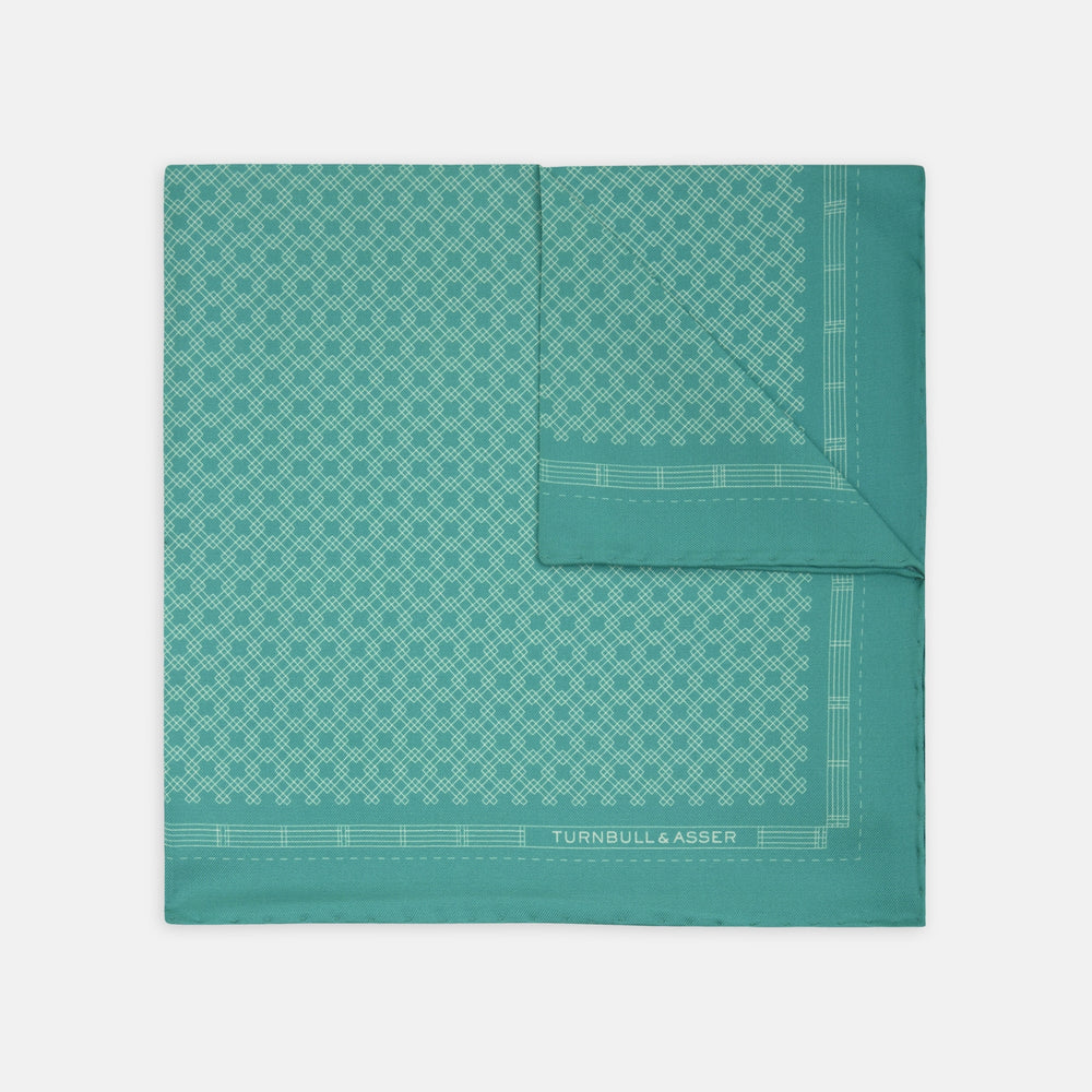 The Kingfisher Green Monocle Silk Pocket Square by Turnbull & Asser features an elegant geometric pattern and border, with the Turnbull & Asser name displayed in white on the lower right corner.