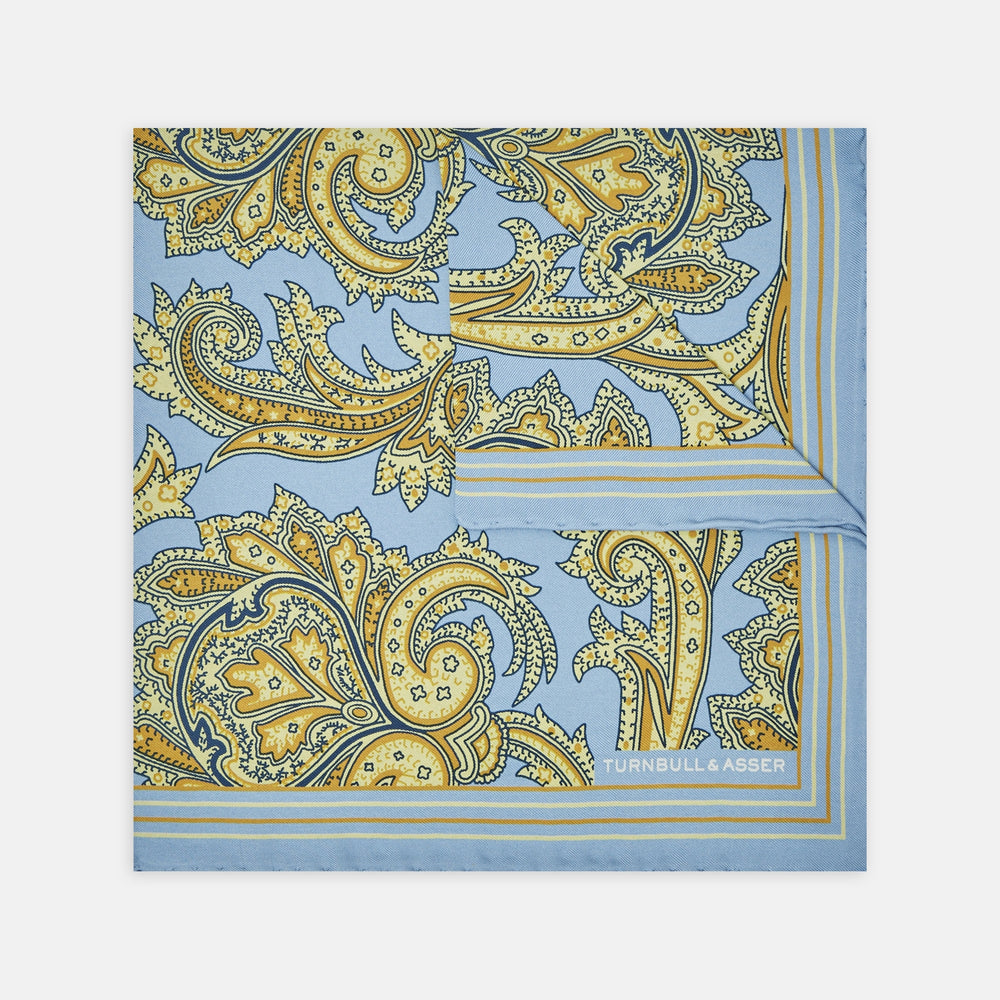 A folded Light Blue and Yellow Large Paisley Silk Pocket Square by Turnbull & Asser features an intricate paisley design. The brand name appears in white on the bottom right corner.