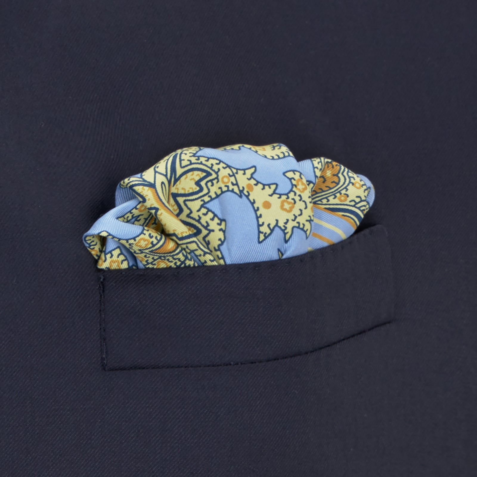 View 4 of product A folded Light Blue and Yellow Large Paisley Silk Pocket Square by Turnbull & Asser features an intricate paisley design. The brand name appears in white on the bottom right corner.