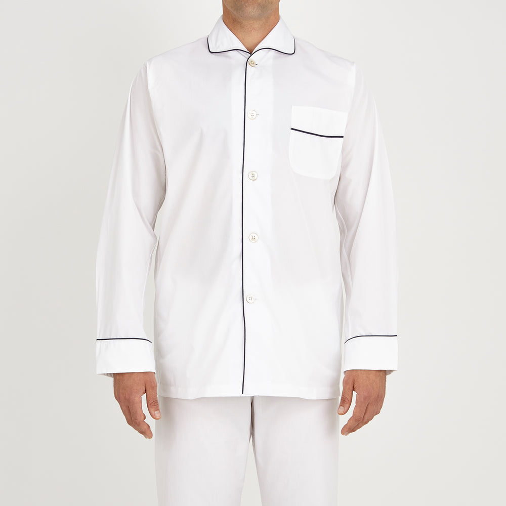 The Turnbull & Asser White Piped Cotton Pyjama Set, made from Egyptian cotton and featuring black piping and two buttons, is shown folded with a matching white tie-strap face mask on a light gray background.