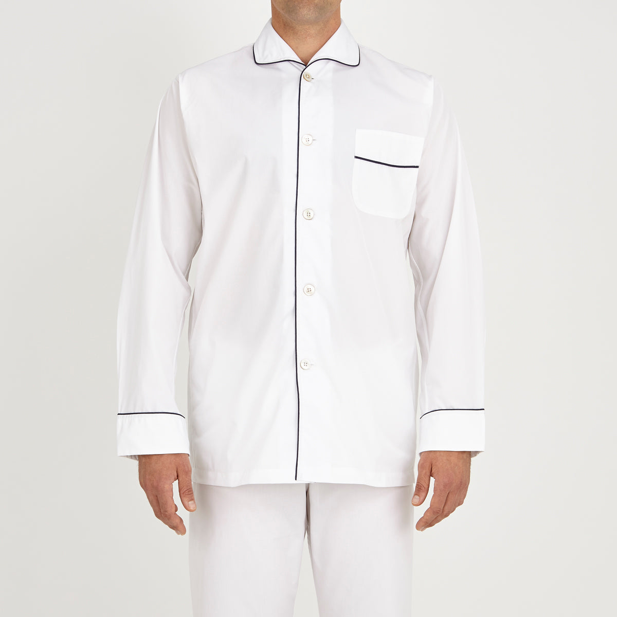 View 2 of product The Turnbull & Asser White Piped Cotton Pyjama Set, made from Egyptian cotton and featuring black piping and two buttons, is shown folded with a matching white tie-strap face mask on a light gray background.