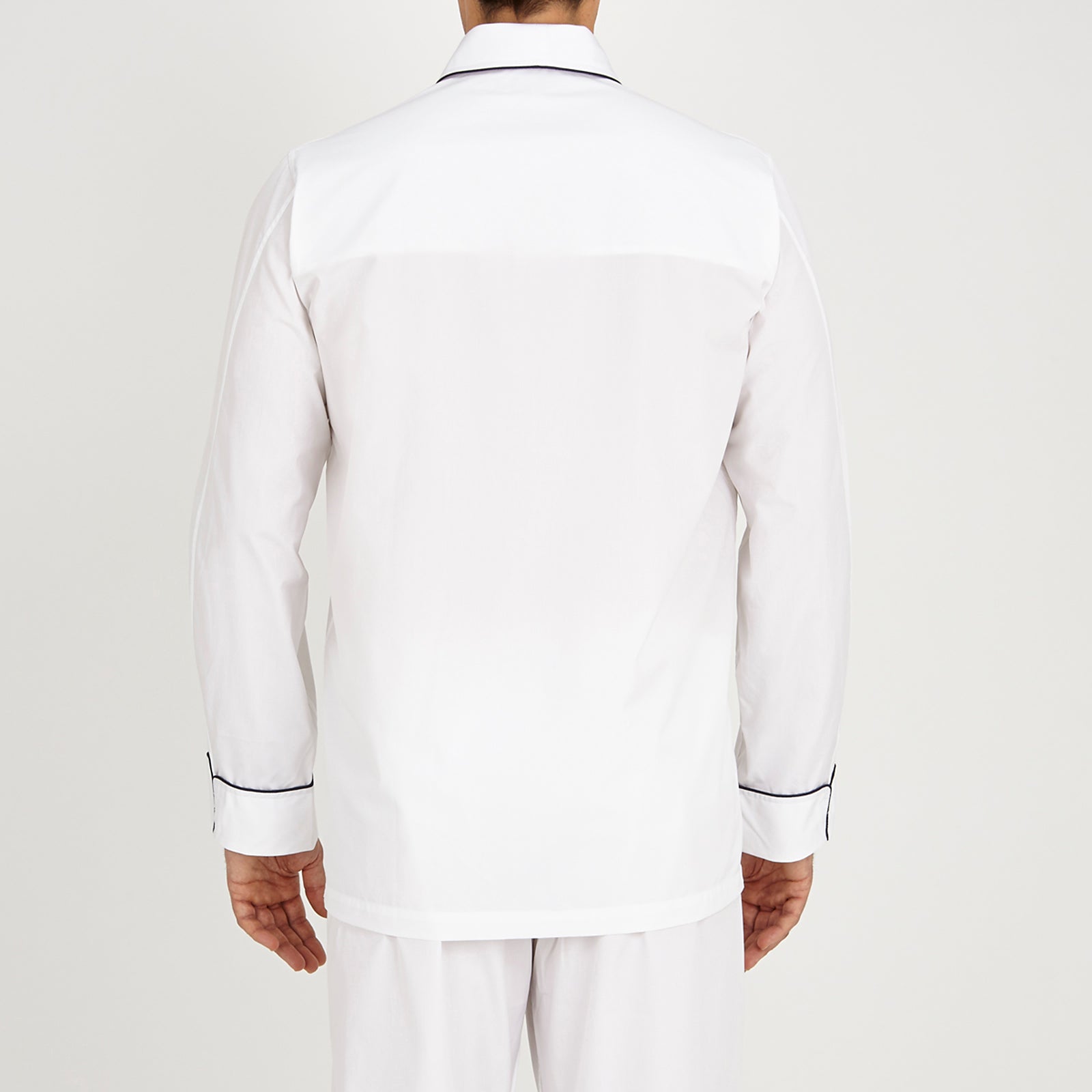 View 3 of product The Turnbull & Asser White Piped Cotton Pyjama Set, made from Egyptian cotton and featuring black piping and two buttons, is shown folded with a matching white tie-strap face mask on a light gray background.