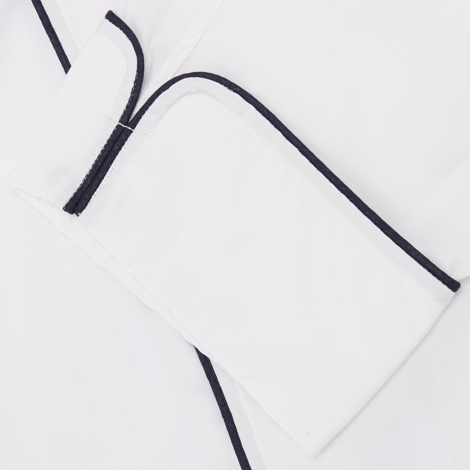 View 4 of product The Turnbull & Asser White Piped Cotton Pyjama Set, made from Egyptian cotton and featuring black piping and two buttons, is shown folded with a matching white tie-strap face mask on a light gray background.