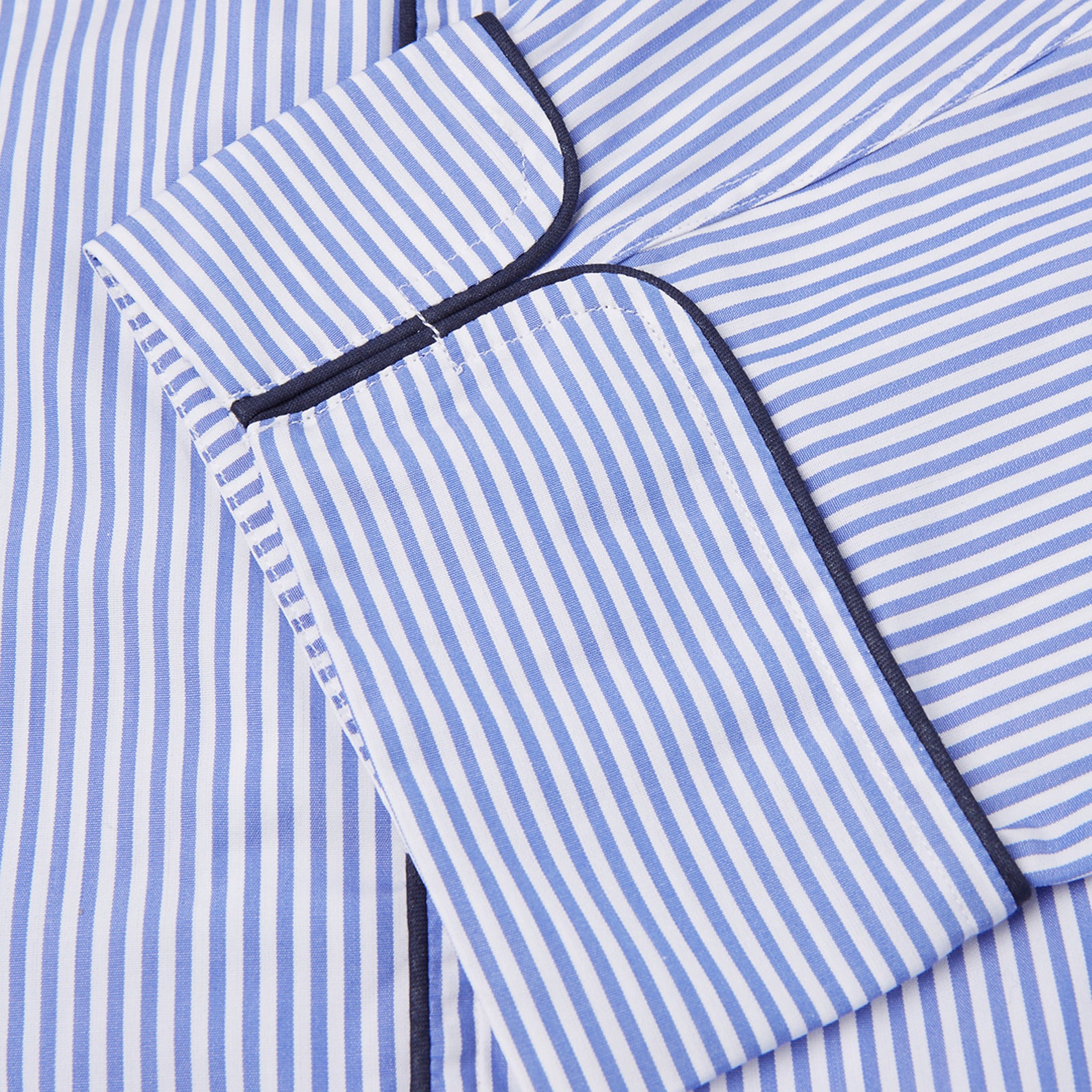 View 4 of product The Turnbull & Asser Blue Bengal Stripe Piped Cotton Pyjama Set, featuring a folded top with white buttons beside matching bottoms, is displayed on a plain light background.