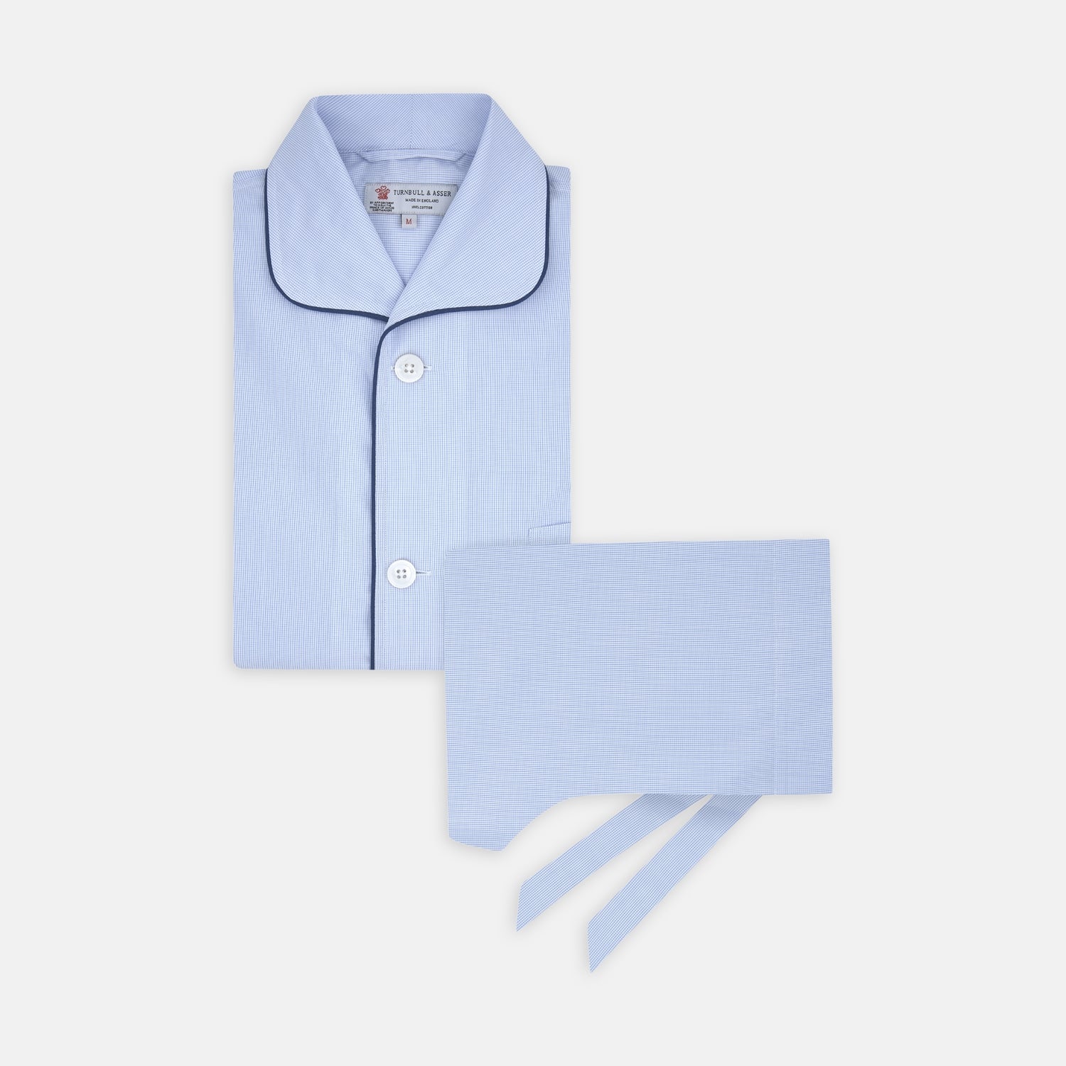 View 1 of product The Turnbull & Asser Light Blue Fine Check Piped Cotton Pyjama Set, crafted from luxurious Egyptian cotton, features a folded top with white buttons, dark piping on the collar, and a matching fabric belt on a plain white background.