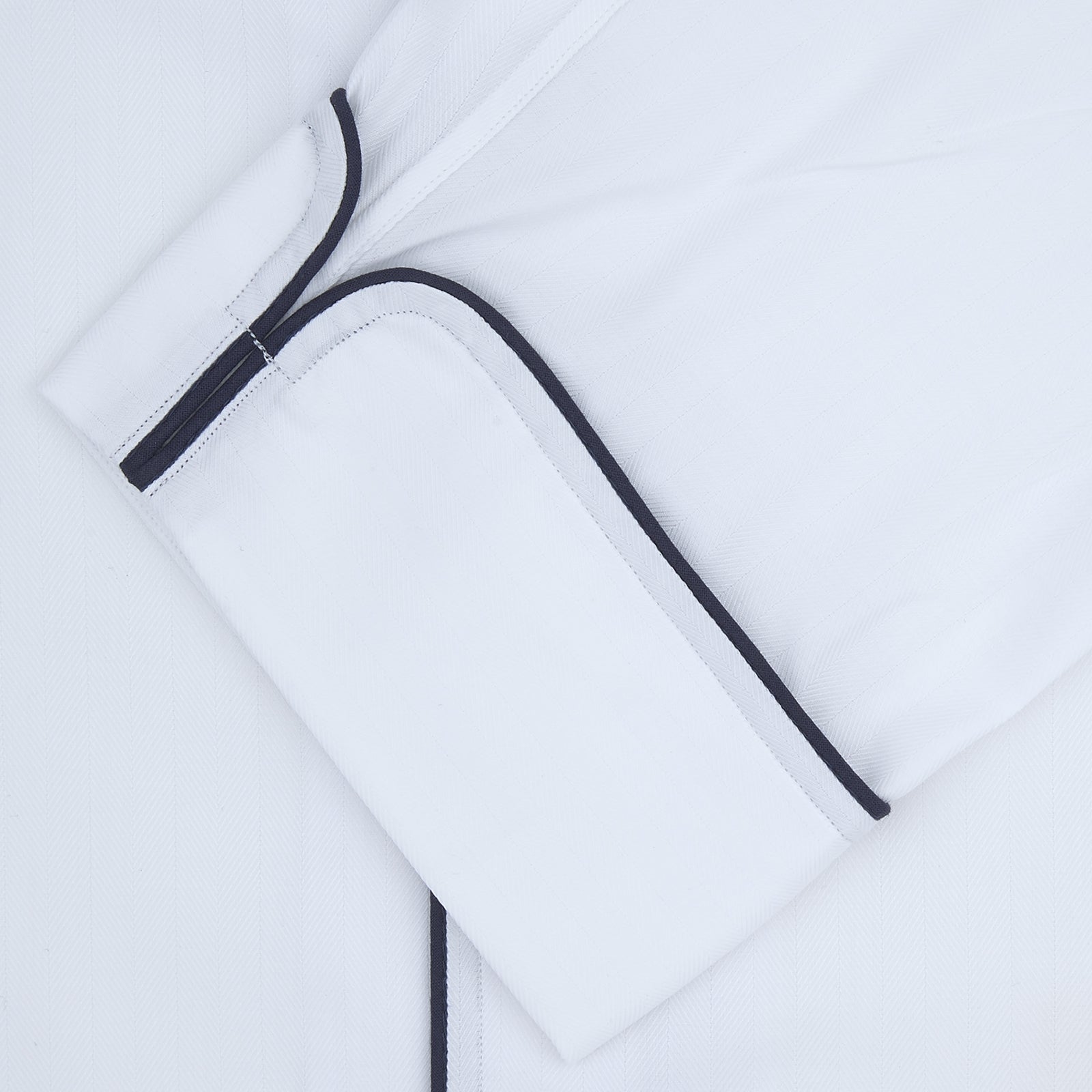 View 2 of product The Turnbull & Asser White Herringbone Piped Superfine Cotton Pyjama Set features a long-sleeve button-up top and drawstring pants with black piping, all crafted from superfine cotton and shown against a plain white background.