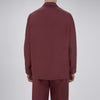 View 3 of product The Wine Piped Silk Pyjama Set by Turnbull & Asser features a folded maroon top with white buttons and dark trim, displayed beside a matching sleep mask with tie straps, set against a plain white background.