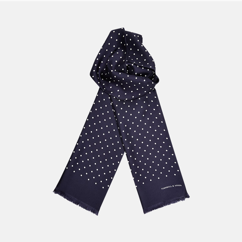 The Navy and White Spotted Silk Scarf by Turnbull & Asser features a hand-printed polka dot design and fringed edges, neatly folded and displayed on a plain white background.