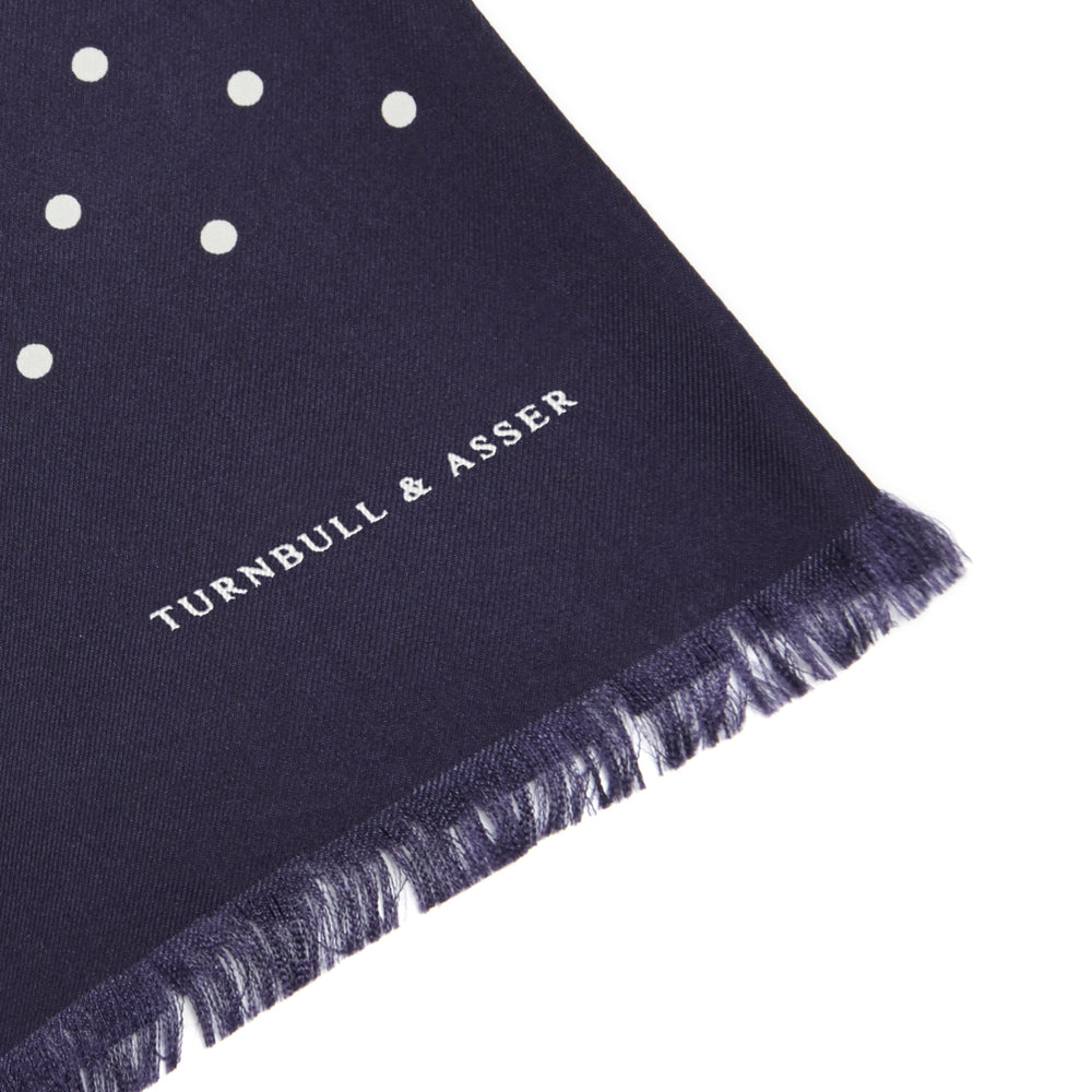 The Navy and White Spotted Silk Scarf by Turnbull & Asser features a hand-printed polka dot design and fringed edges, neatly folded and displayed on a plain white background.