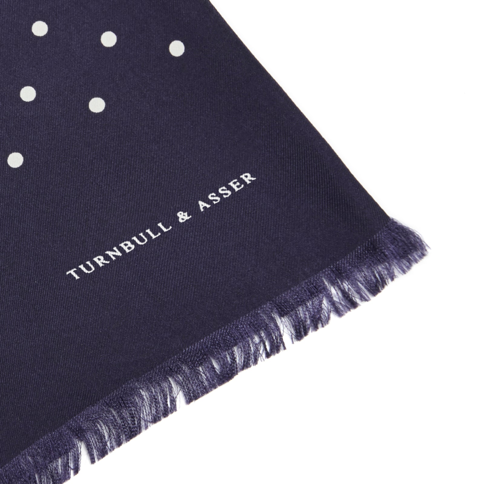 View 2 of product The Navy and White Spotted Silk Scarf by Turnbull & Asser features a hand-printed polka dot design and fringed edges, neatly folded and displayed on a plain white background.