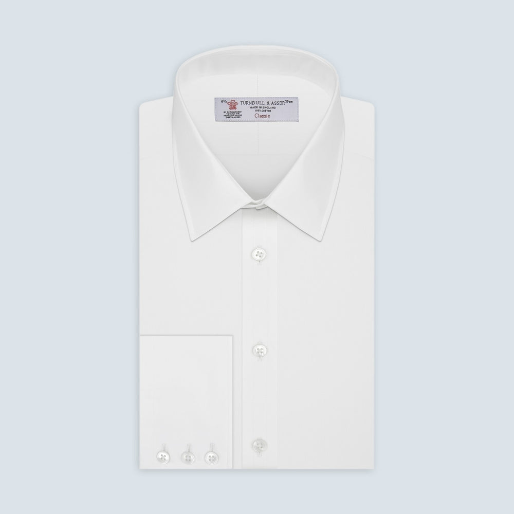 A circular swatch of Turnbull & Asser’s Plain White Cotton Fabric is shown against a light gray background, highlighting its smooth texture and a subtle stitched edge on the right side.