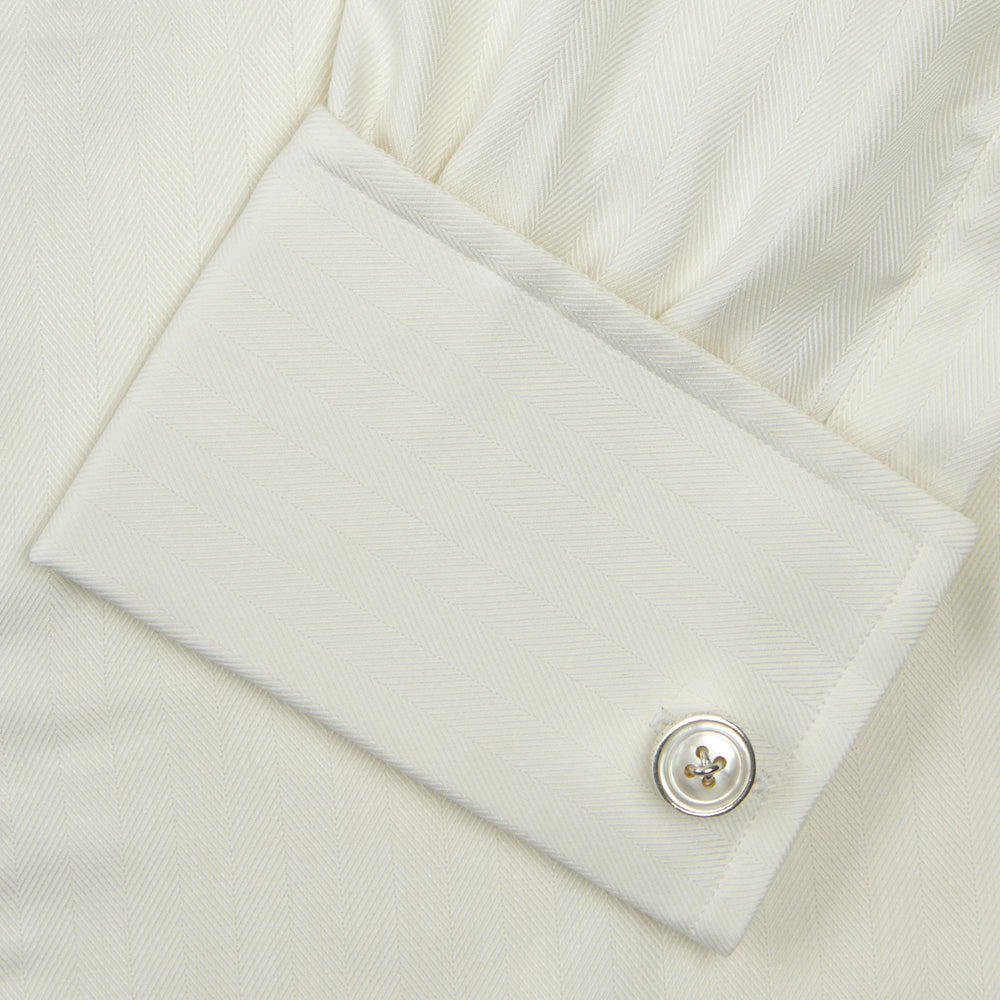 The Turnbull & Asser Cream Herringbone Superfine Cotton Shirt features a T&A collar, double cuffs, and a subtle pattern. It is neatly folded with white buttons and displayed on a plain white background.