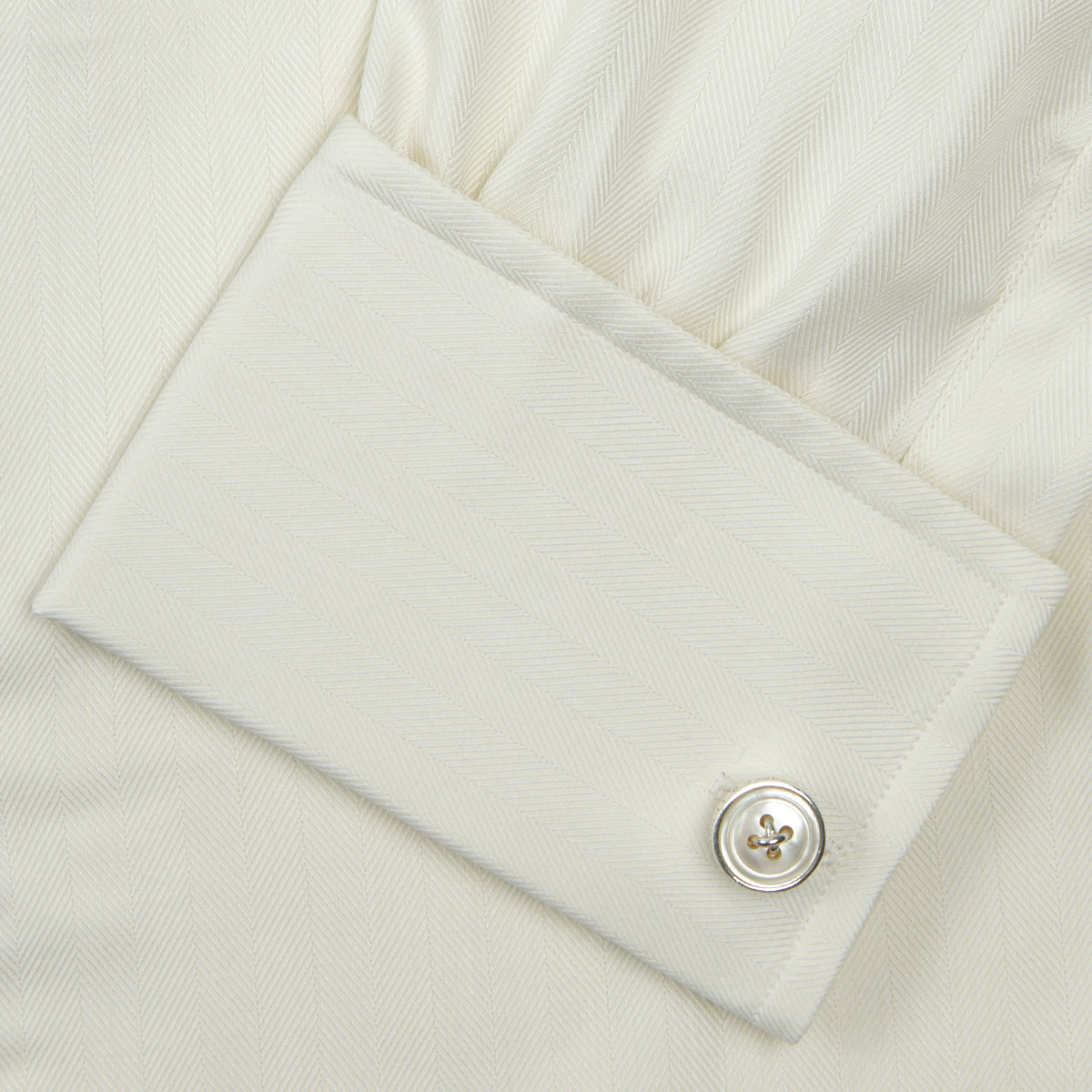 View 6 of product The Turnbull & Asser Cream Herringbone Superfine Cotton Shirt features a T&A collar, double cuffs, and a subtle pattern. It is neatly folded with white buttons and displayed on a plain white background.