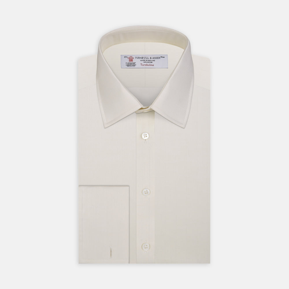 The Turnbull & Asser Cream Herringbone Superfine Cotton Shirt features a T&A collar, double cuffs, and a subtle pattern. It is neatly folded with white buttons and displayed on a plain white background.