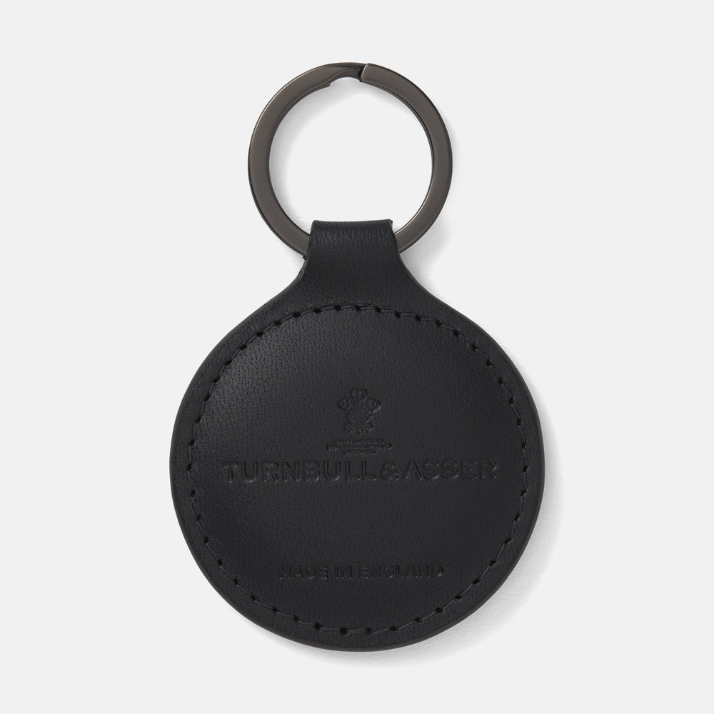 The Black Leather Key Fob from Turnbull & Asser features a round black leather design with a metal ring, embossed with the brand logo and "MADE IN ENGLAND"—an elegant key accessory for any collection.