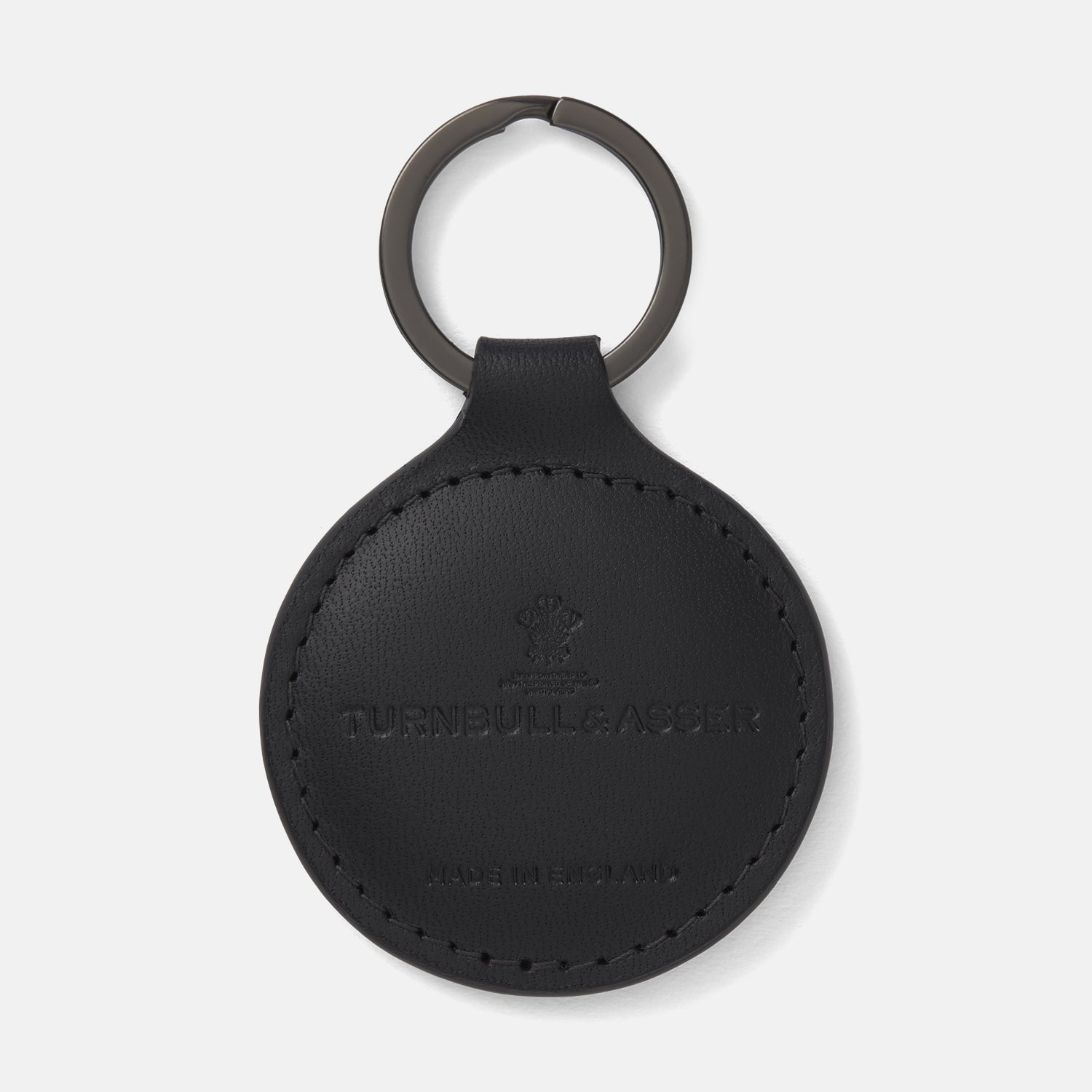 View 1 of product The Black Leather Key Fob from Turnbull & Asser features a round black leather design with a metal ring, embossed with the brand logo and "MADE IN ENGLAND"—an elegant key accessory for any collection.