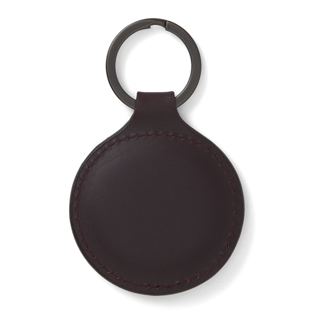 The Violla Leather Key Fob by Turnbull & Asser is a round, dark brown leather accessory with embossed branding, visible edge stitching, and a metal loop at the top. Made in England, it combines elegance and function for your keys.