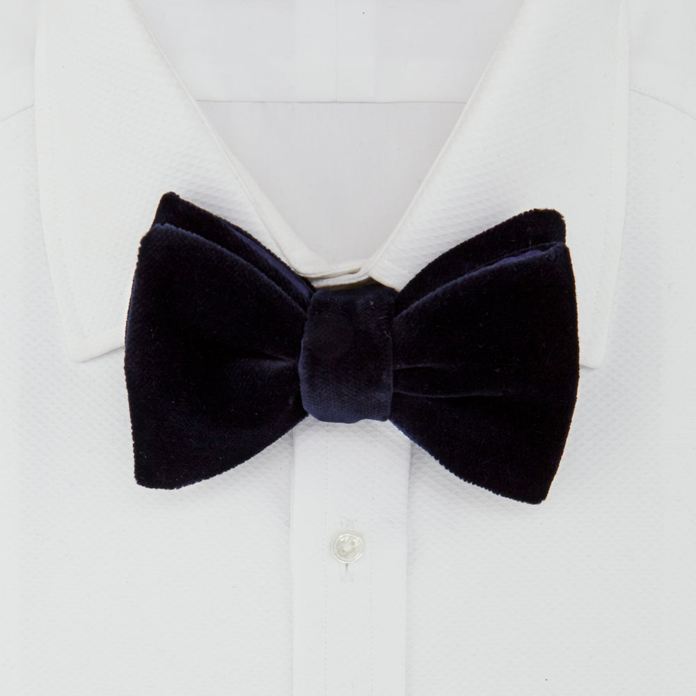 The Turnbull & Asser Navy Velvet Bow Tie, crafted from plush velvet, is shown against a white background—an elegant choice for formal occasions.